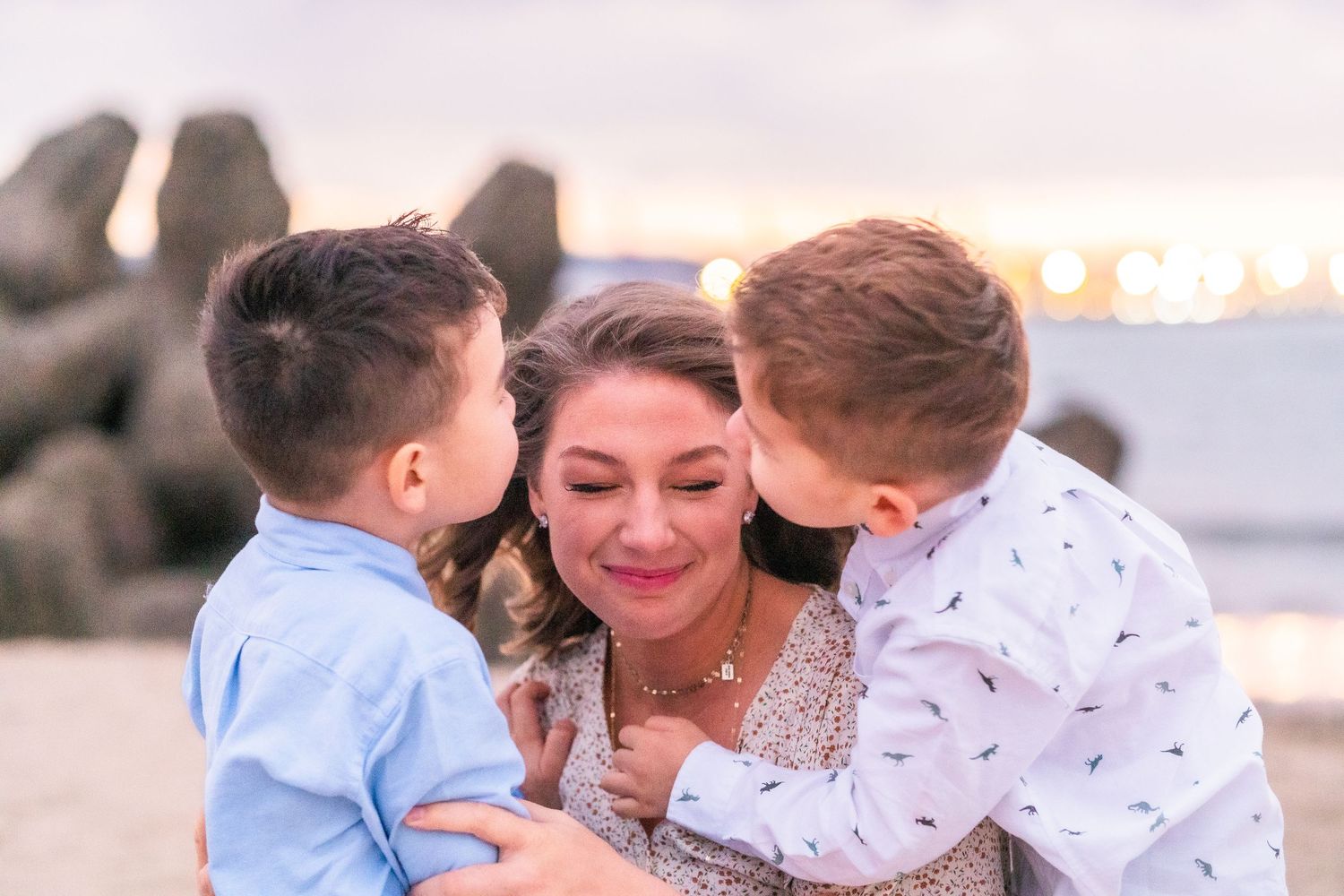 Family sharing tender moment together at sunset near ocean rocks.