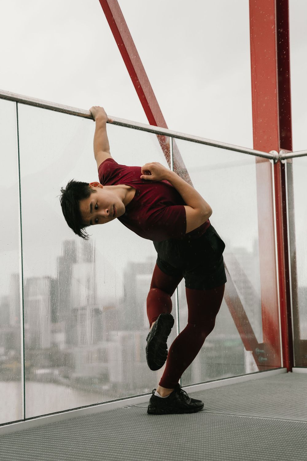 Athletic figure performs artistic bend pose against city skyline through glass barrier.