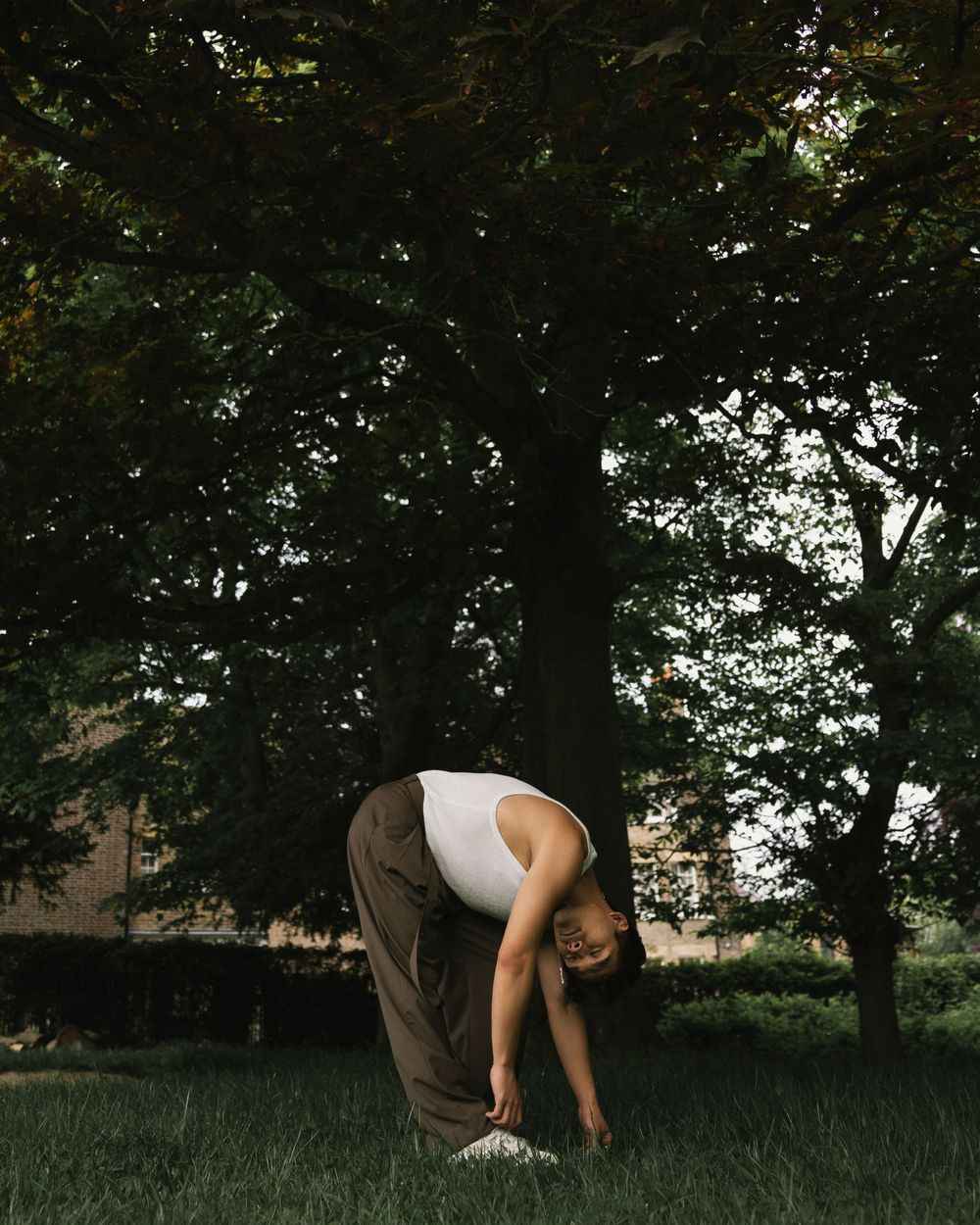 Figure in athletic wear stretches forward under lush green tree canopy.