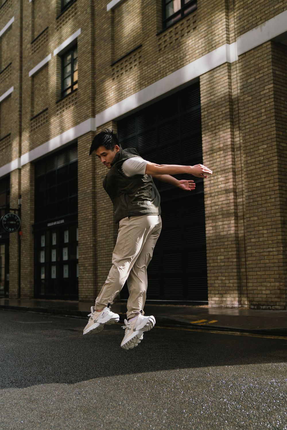 Person in casual wear performing mid-air jump on urban street with brick building backdrop.