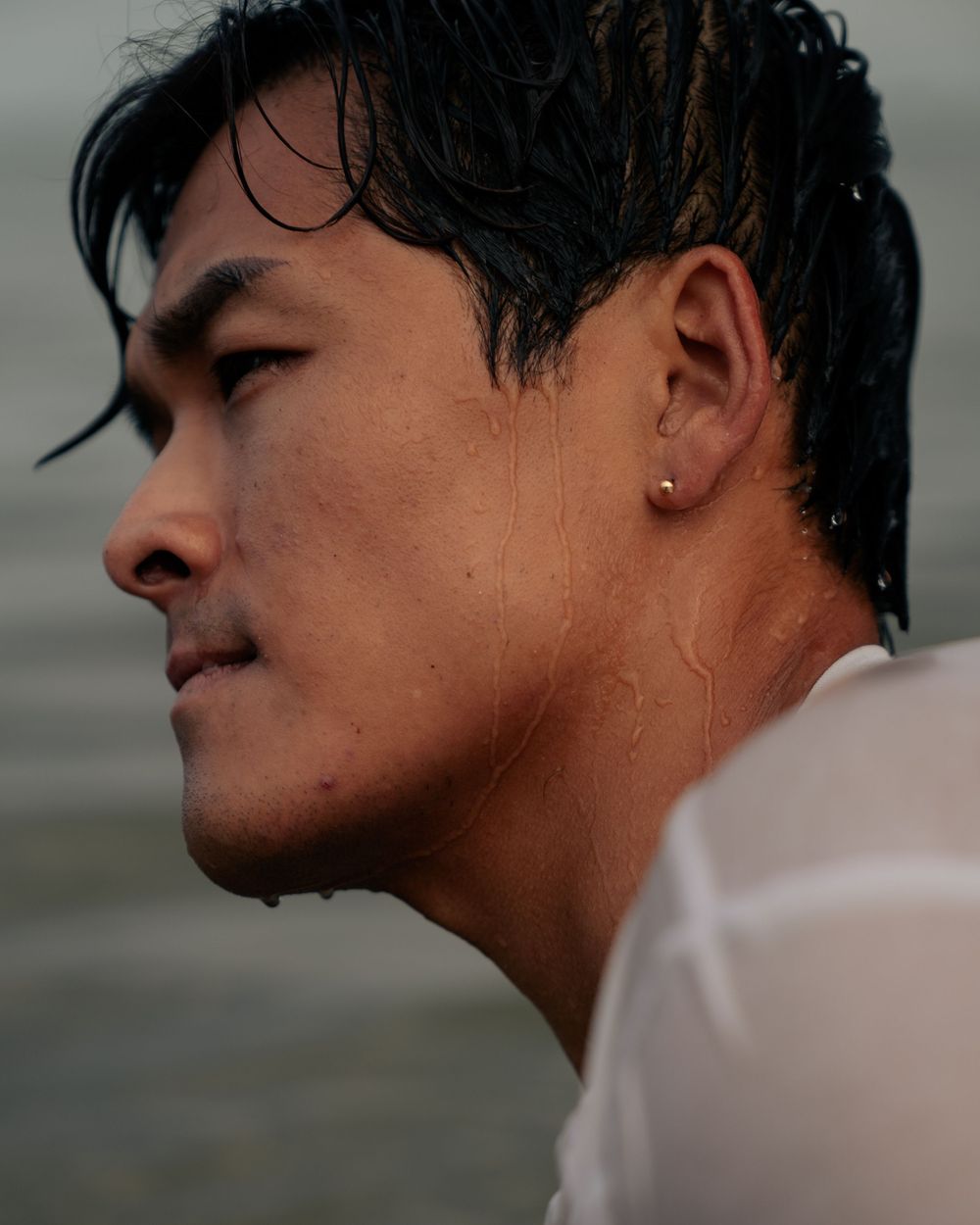 A profile view captures wet hair and an earring against a moody gray background.