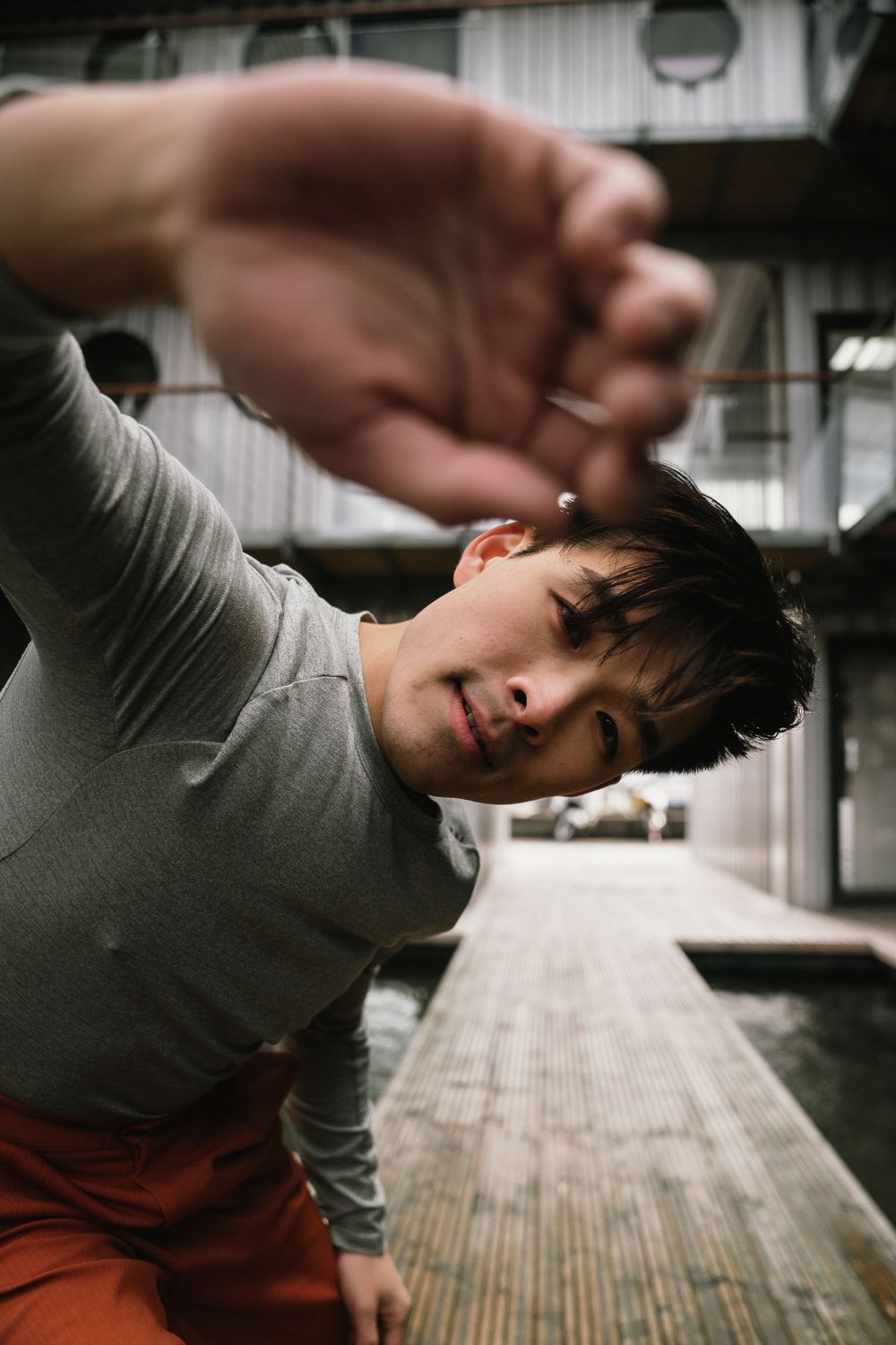 Person in grey shirt and orange pants performs expressive dance move outdoors.