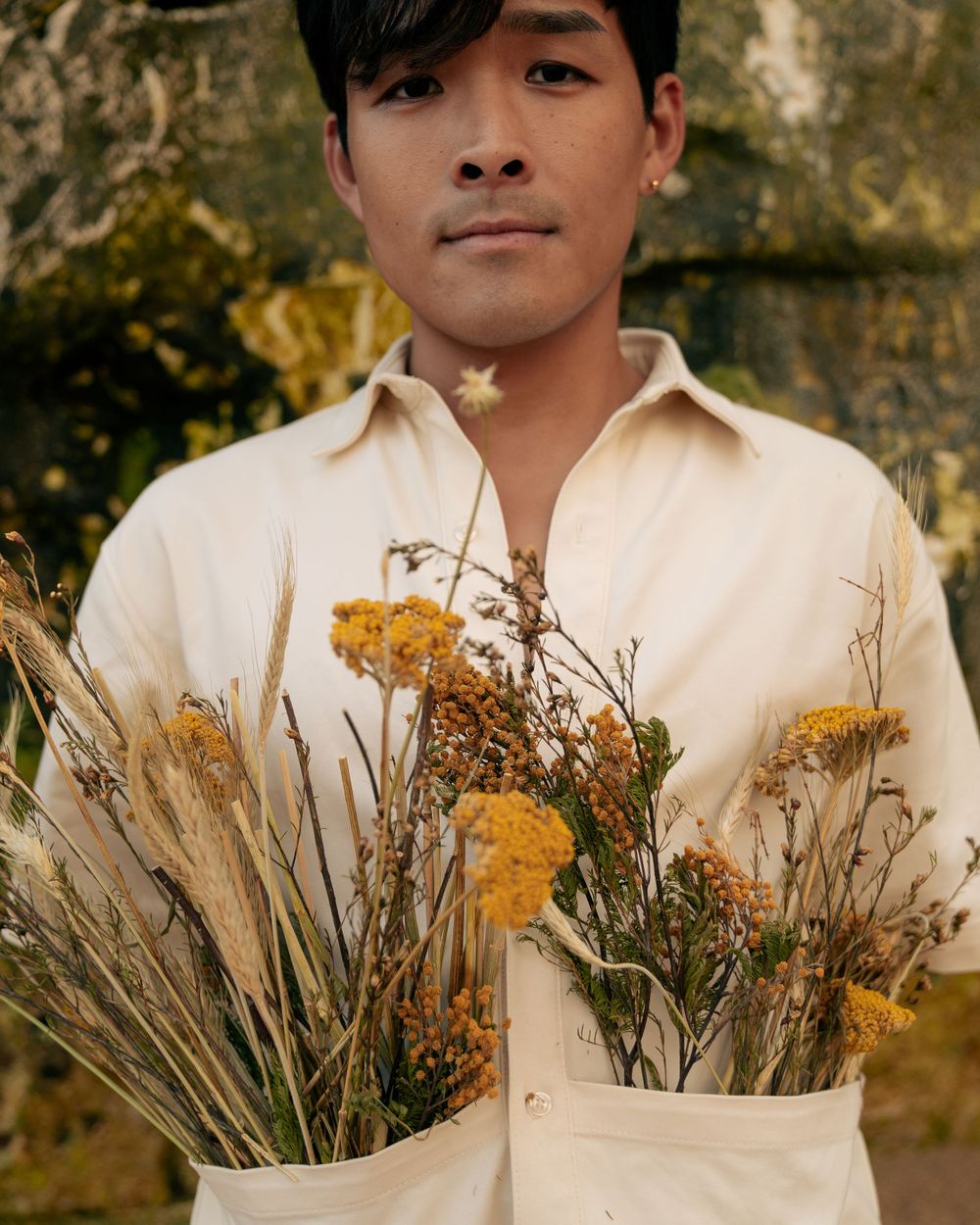 A white collared shirt adorned with dried wildflowers and grasses creates a natural composition.