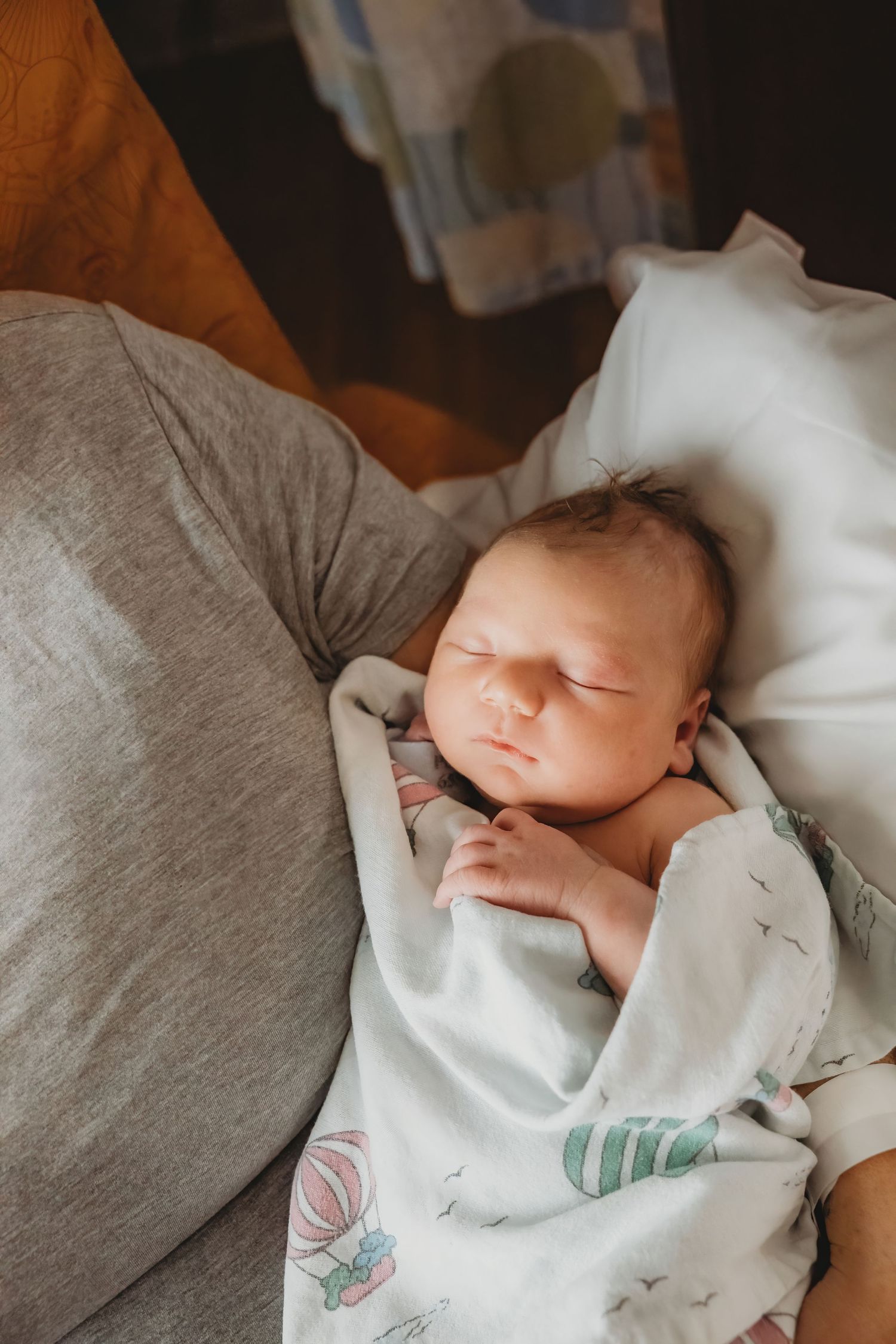 A peaceful sleeping newborn swaddled in white with balloon print blanket.