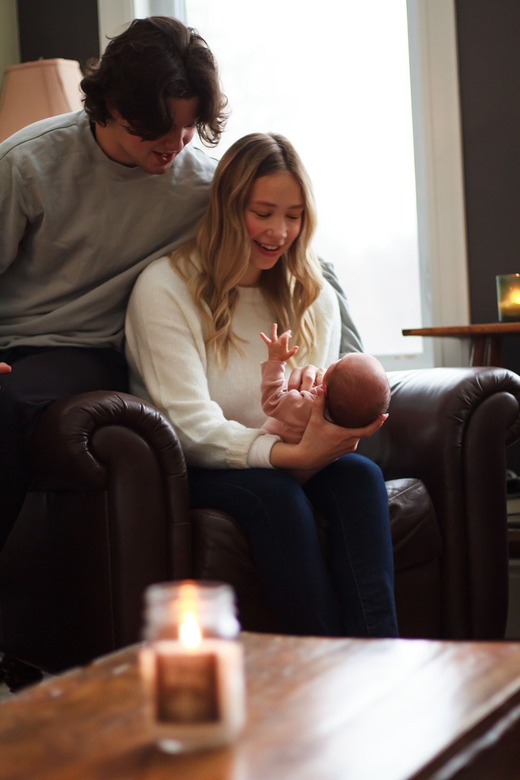 New parents sit on couch admiring newborn in llifestyle session.
