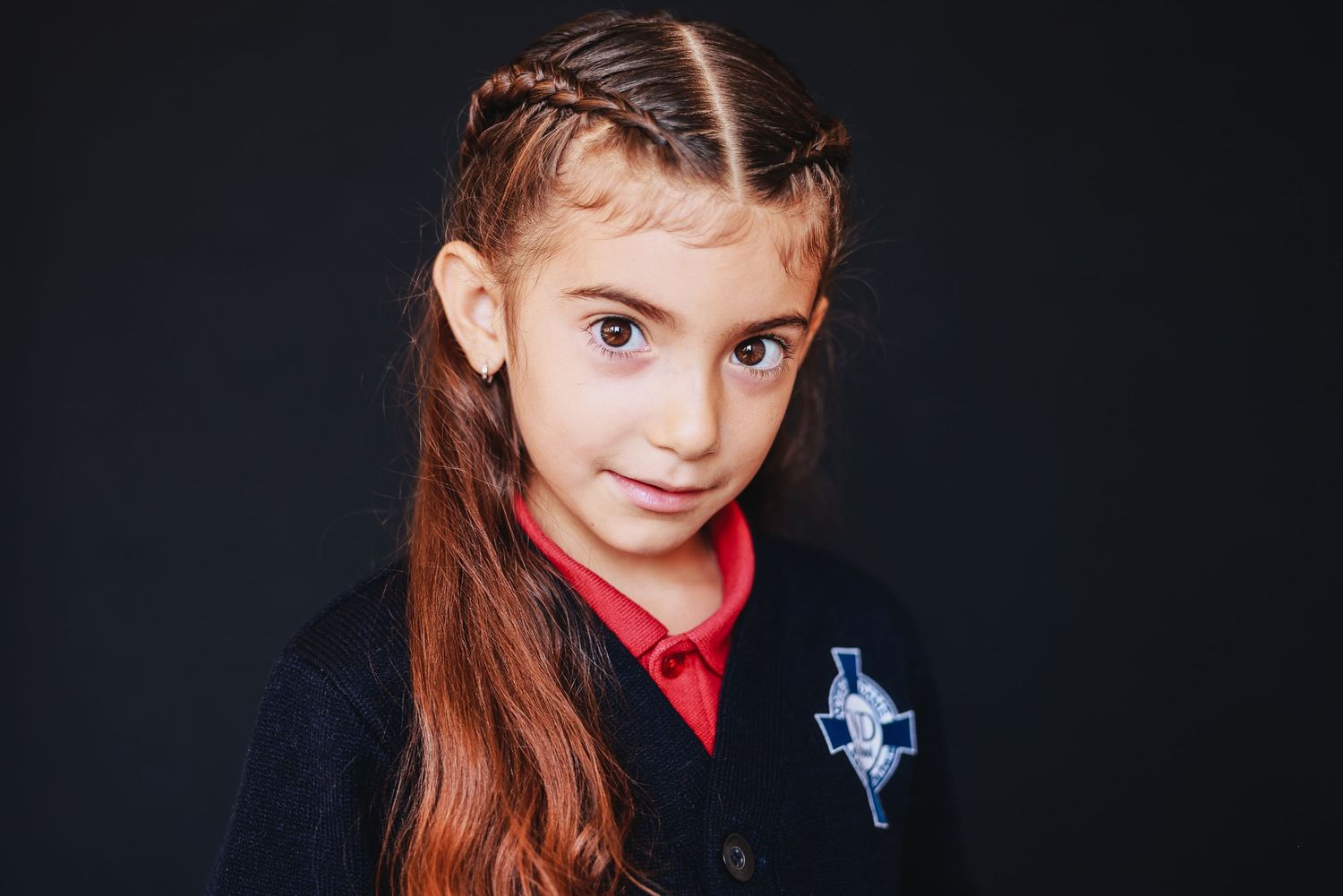 Young student in navy uniform with red collar and braided hair.