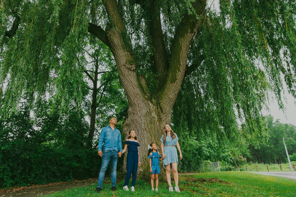 A family stands together under a large weeping willow tree in a green park setting.