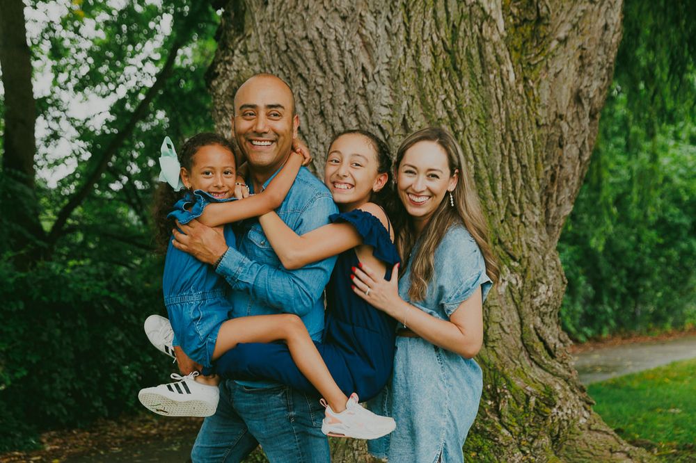 A cheerful family poses together for a portrait in front of a massive tree trunk.