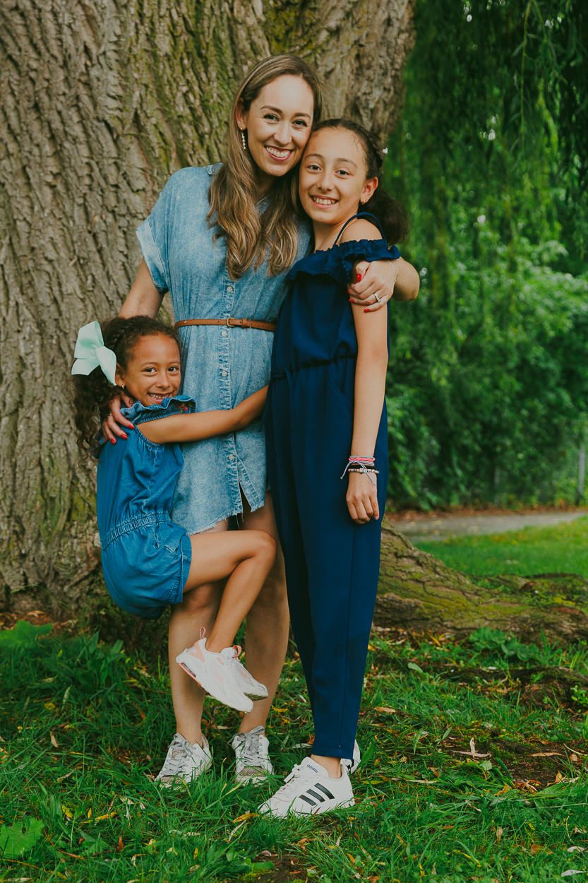 Three people in coordinating blue outfits pose casually against a large tree trunk outdoors.