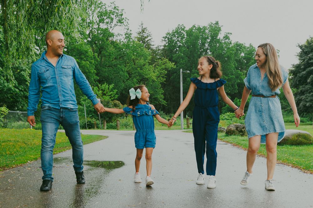 A family walking and holding hands on a wet path through a green park.