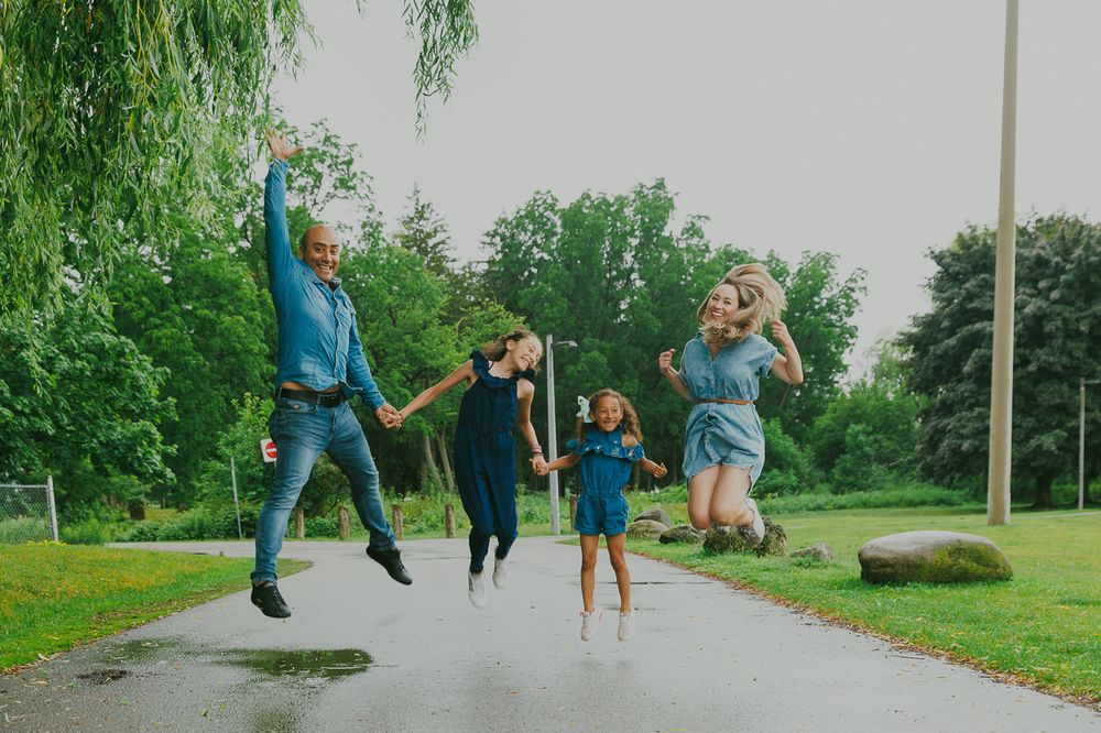 Family members jumping with joy on a park path surrounded by green trees.