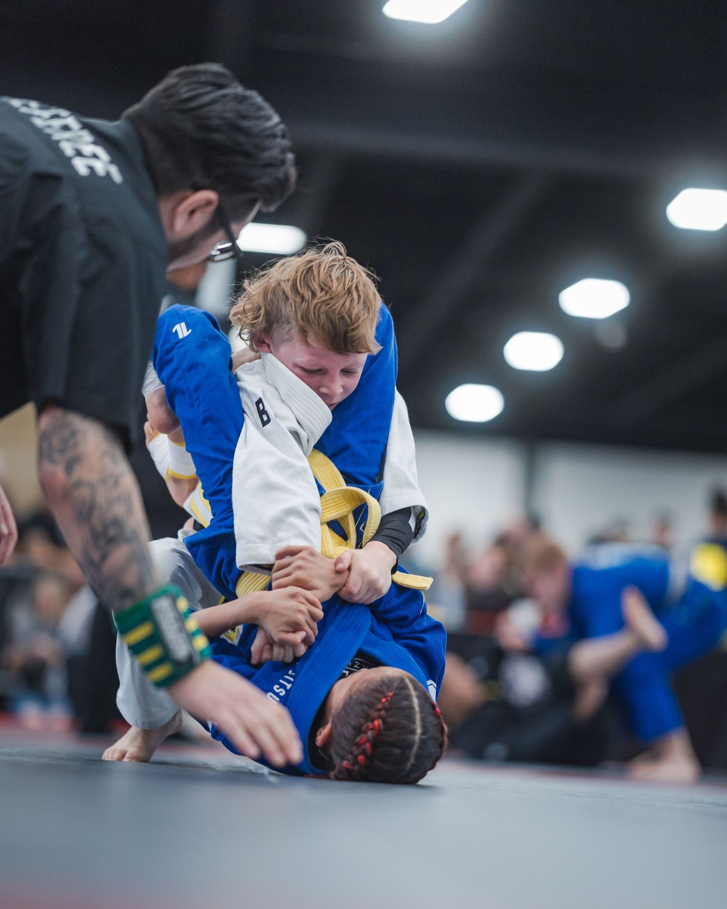 Two martial artists grappling during a competition on blue mats.