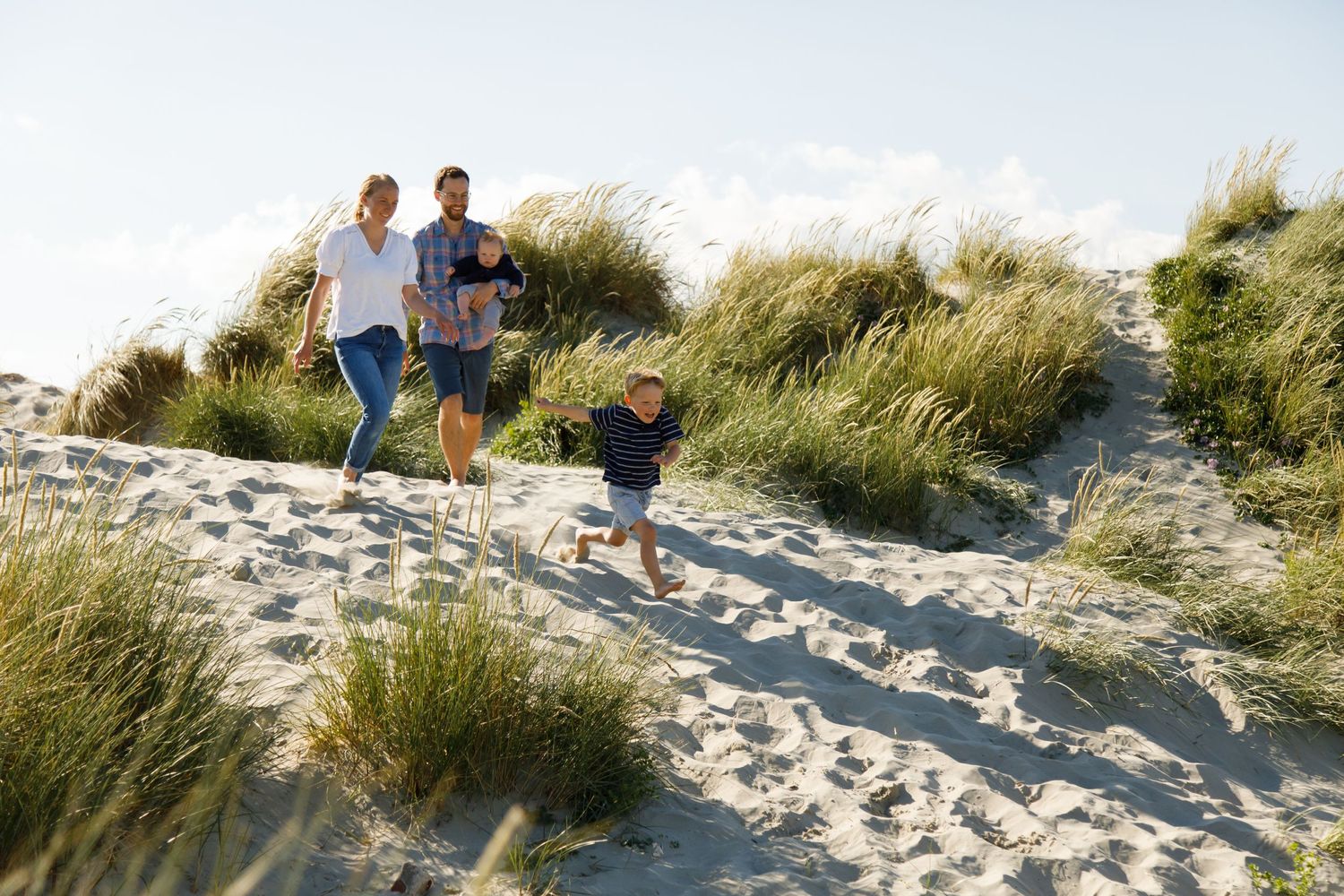 Family walking and playing together on sandy beach dunes during golden hour during a family beach photoshoot