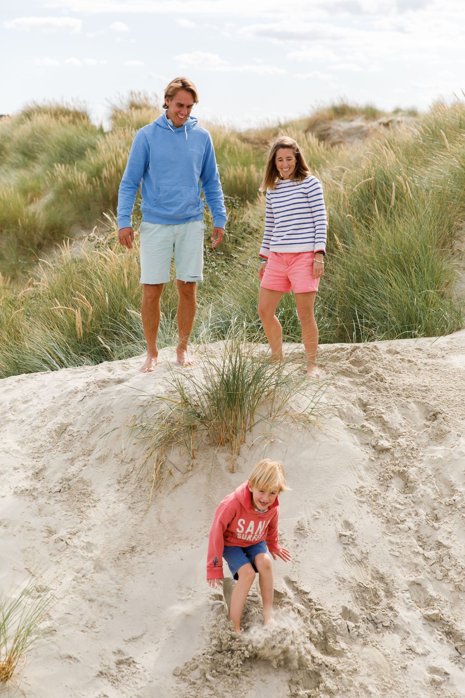 Three people enjoying a playful moment on sandy dunes covered with beach grass during a family beach photoshoot