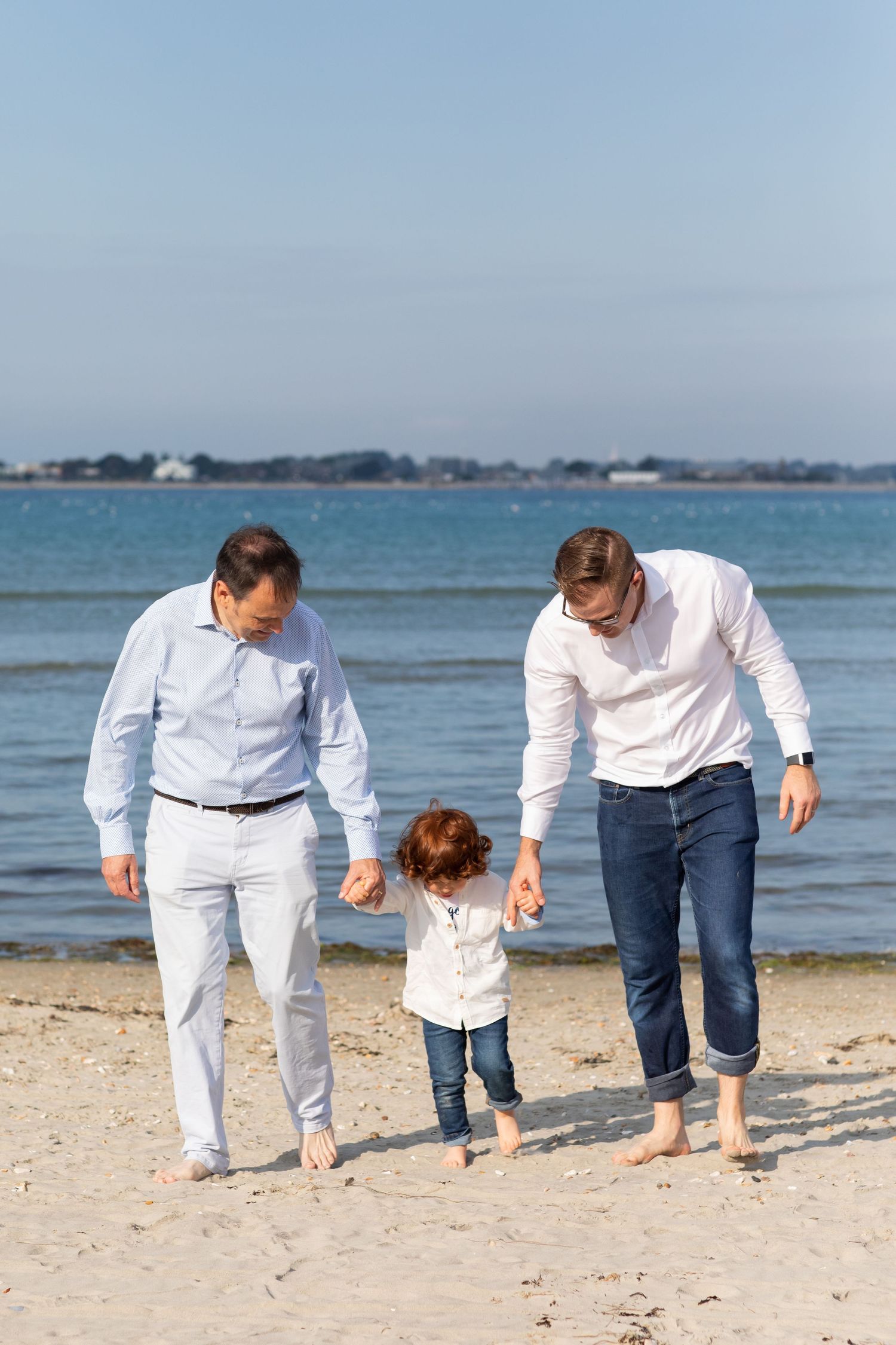 Three people walking together on a sunny beach with calm ocean in background during a family beach photoshoot