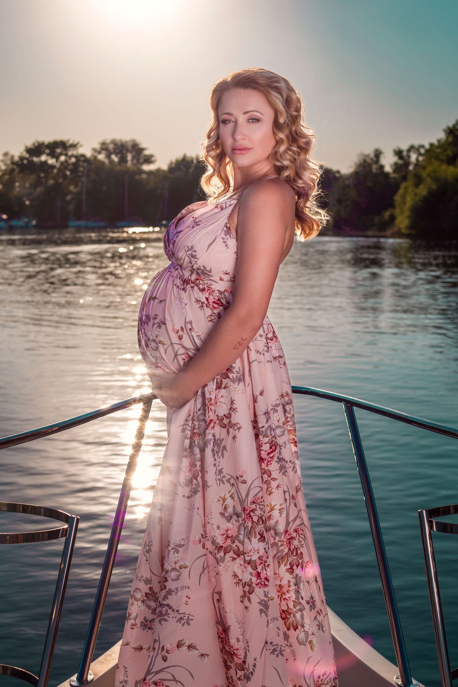 Maternity photoshoot on a boat at sunset featuring a floral dress and waterfront scenery.