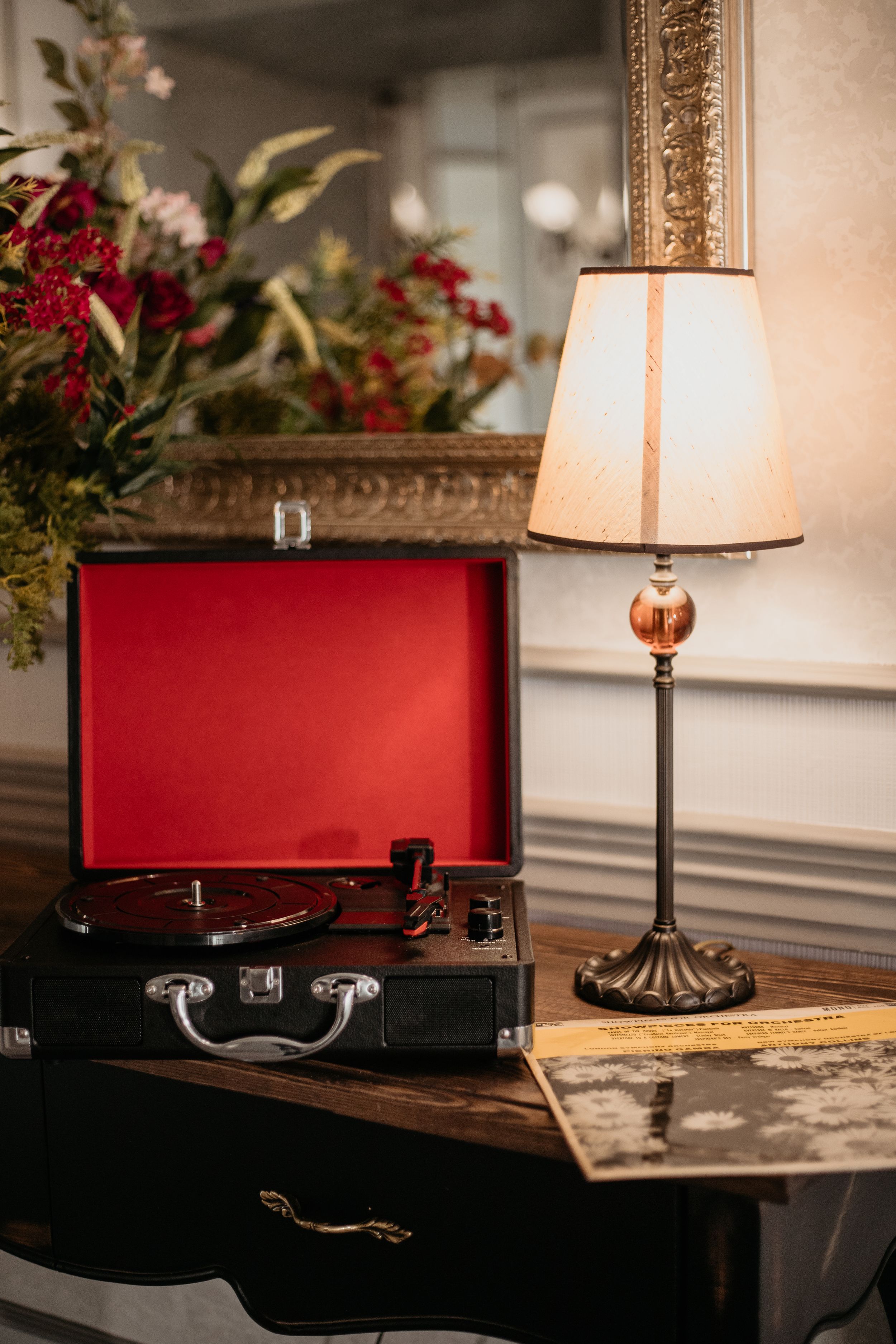 Vintage record player and table lamp displayed with red floral arrangement in an elegant setting.