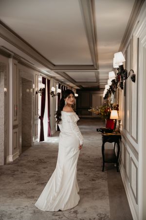 Elegant bride in fitted white gown poses in a luxurious hotel corridor.