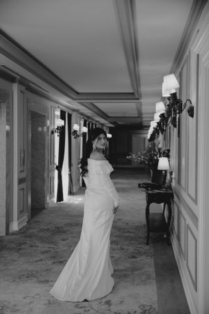 Black and white photo of someone in a wedding gown walking down an elegant hallway.