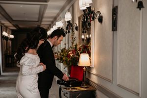 Elegant couple examining decorative details in luxurious hotel corridor with vintage lighting.