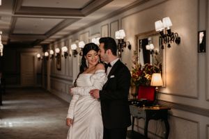 Couple embracing in elegant hallway with vintage wall sconces and classical decor.