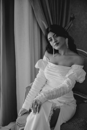 Black and white portrait of woman in white dress with long sleeves against window light.