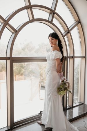 Full-length bridal portrait featuring fitted white gown against arched window backdrop.