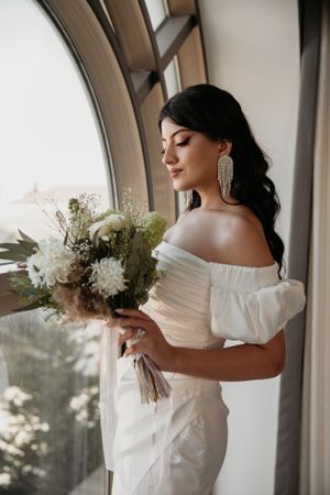 Serene bridal portrait with white bouquet against dramatic arched window.
