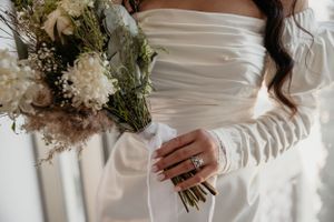 Close-up of a bride holding a delicate dried flower bouquet with white blooms and greenery.