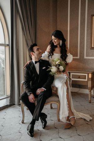 Romantic wedding portrait with couple by arched window in elegant formal attire.