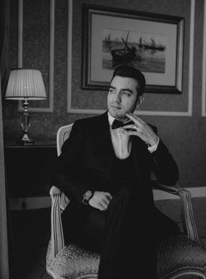 Classic black and white portrait of groom in formal attire with vintage decor and artwork.