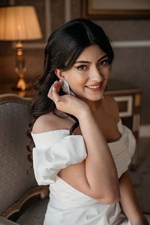An elegant bridal portrait featuring a bride in a white off-shoulder dress with statement earrings in a luxurious setting.