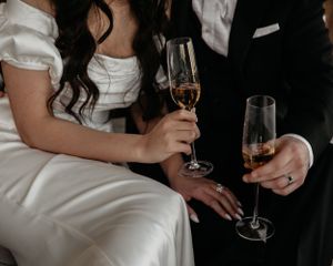 Close-up shot of champagne glasses held by a couple in wedding attire during an intimate celebration.