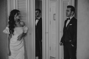 A black and white wedding photo capturing a moment between doors in a classic hotel hallway.