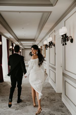 A candid wedding photo of a couple walking down an elegant hotel hallway with classic wall sconces.