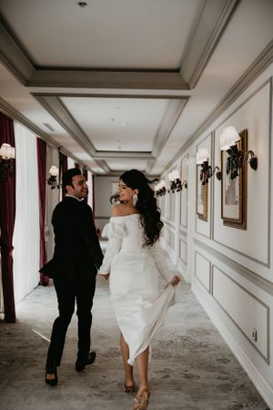 A romantic moment captured of a couple walking down a luxurious corridor in formal wedding attire.