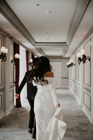 Couple in wedding attire walking through an elegant hallway with classic wall sconces.