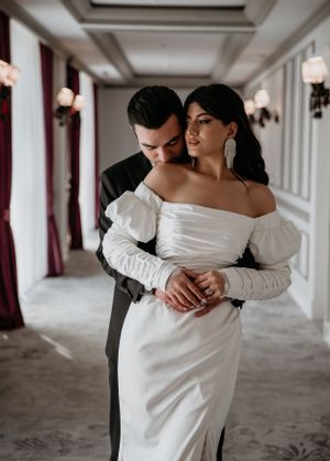 Tender moment between a couple in formal attire standing in an upscale hotel hallway.