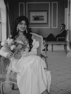 Black and white portrait of person holding floral bouquet in vintage-style chair.