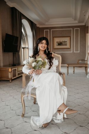 Elegant bridal portrait in a luxurious room with person holding white floral bouquet.