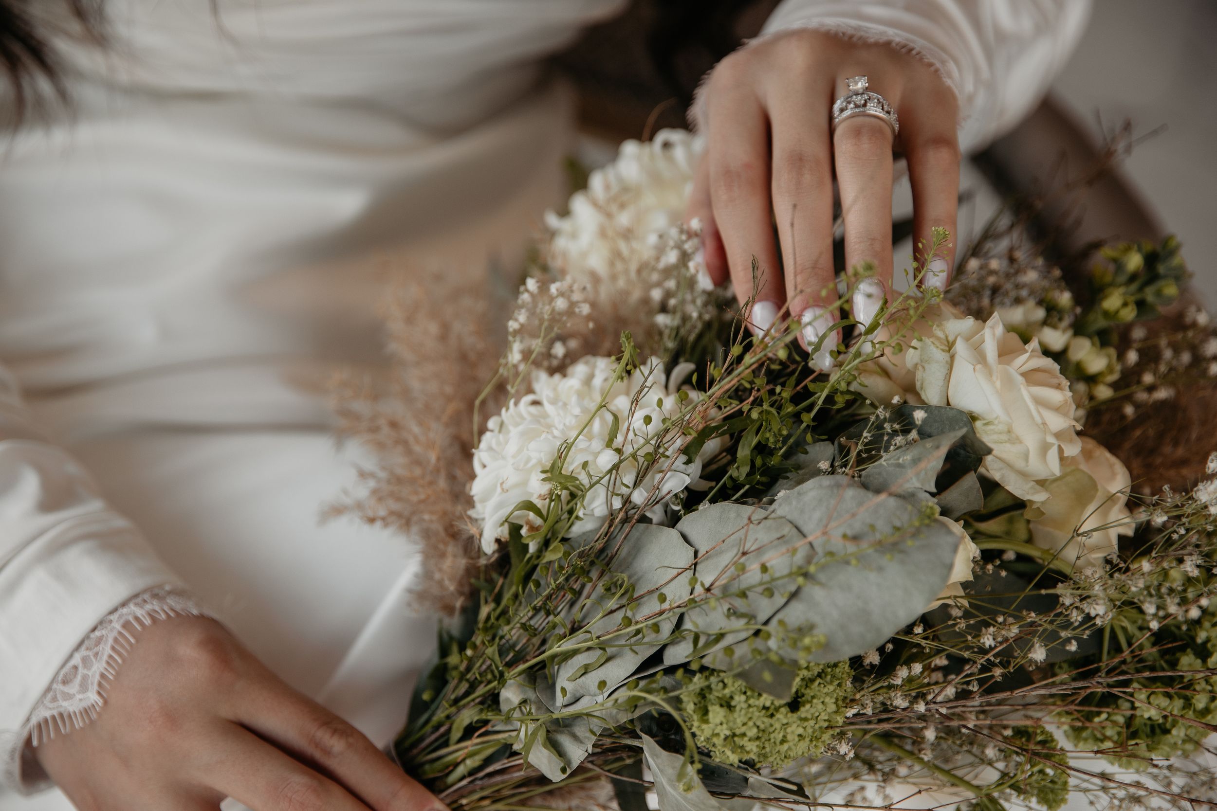 Close-up shot of hands holding a white and green dried flower bouquet with a sparkling ring.