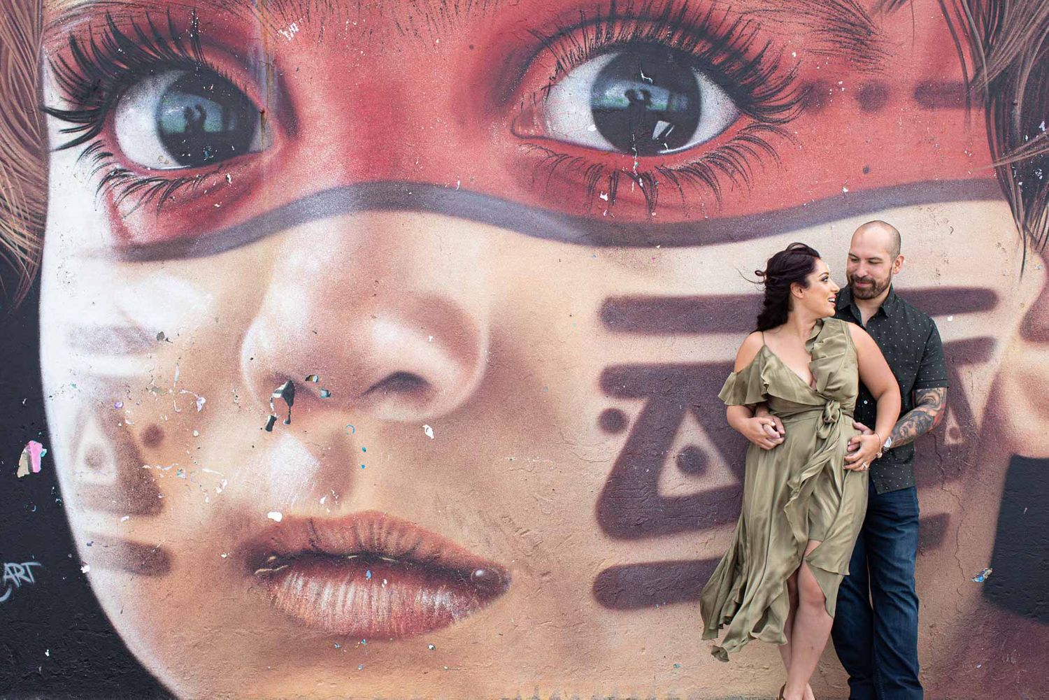 Large scale street art mural featuring close-up eyes and face details.