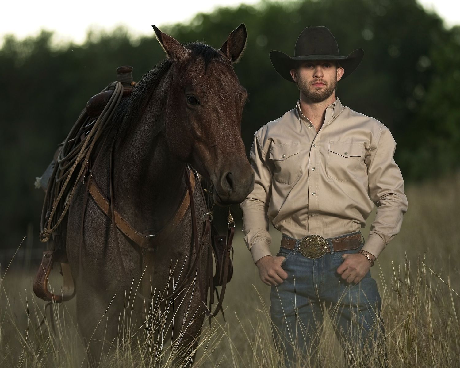 Leighton Berry poses with his horse in a field of high grass.