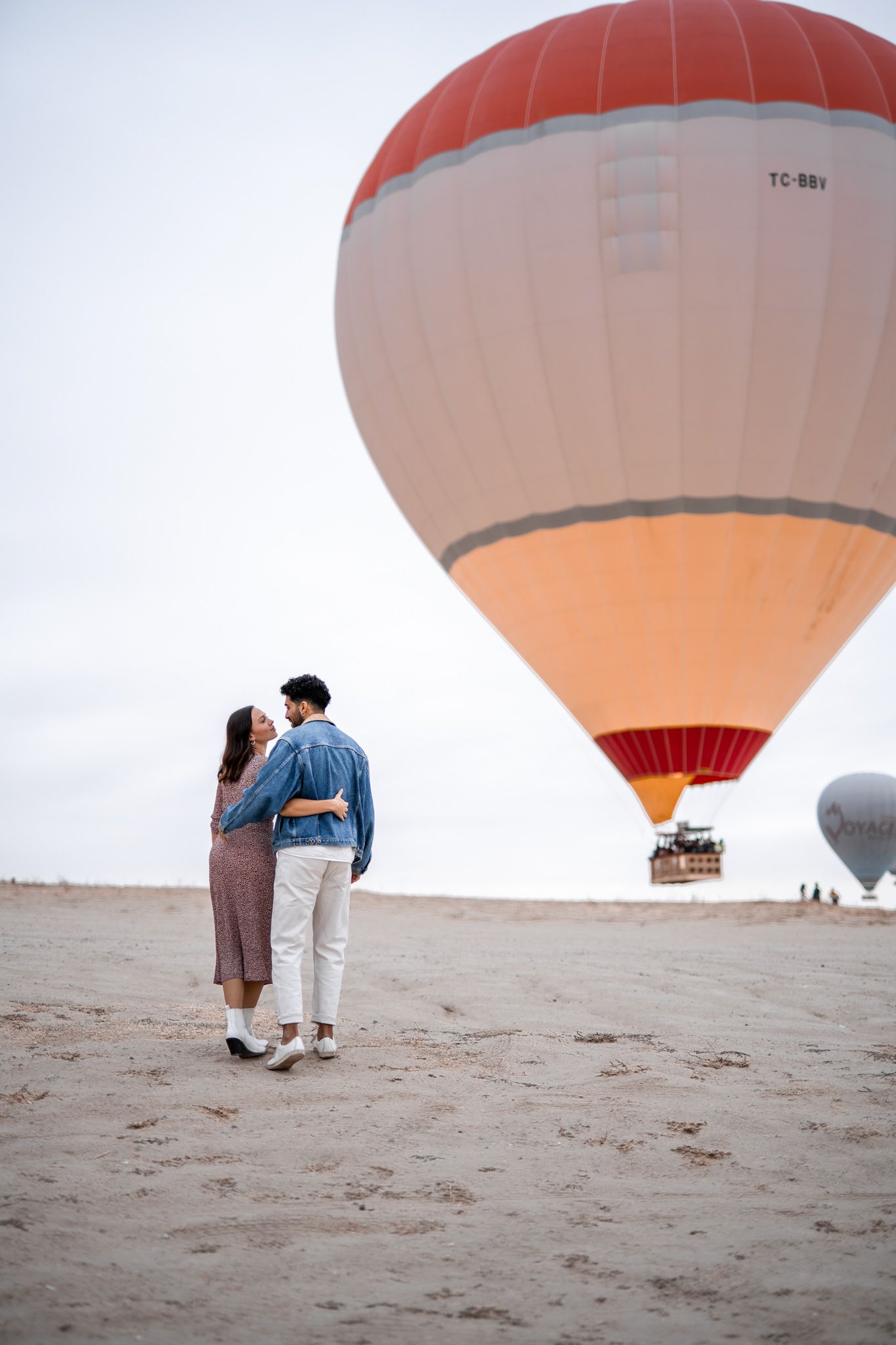 Romantic couple strolling on beach near large peach-colored hot air balloon.