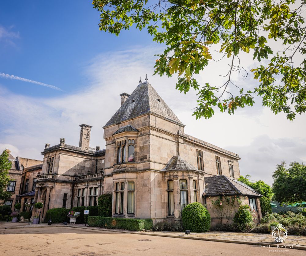 Elegant Victorian mansion with ornate architecture and landscaping against blue sky on sunny day.