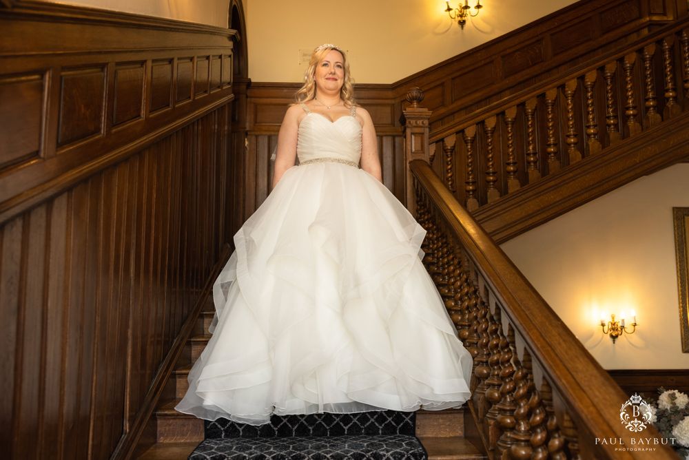 A strapless white wedding gown with voluminous tulle skirt displayed on an elegant staircase.