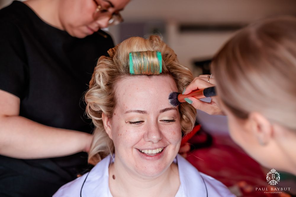 Wedding makeup application being done while hair is set in rollers during morning preparations.