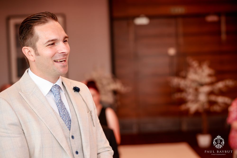 A wedding ceremony participant in a light beige suit and blue tie smiles warmly.