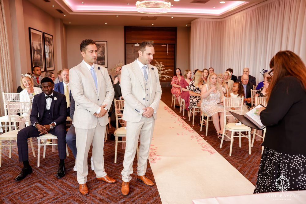 Wedding guests await ceremony in elegant banquet room with white decor and pink lighting.