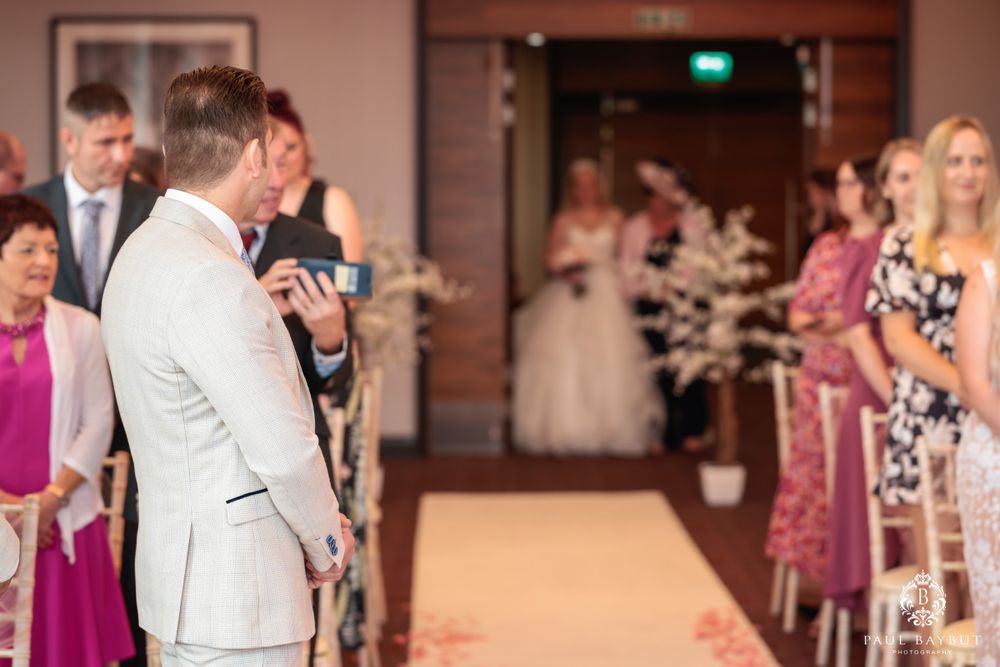 Wedding ceremony taking place in elegant ballroom with pink walls and white aisle runner.